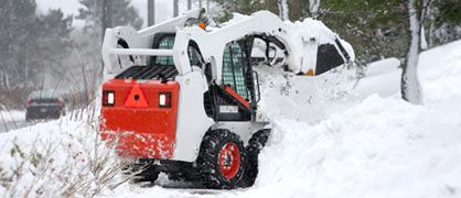 A skid steer removing snow on the side of a road